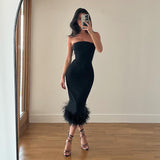 Woman wearing a black strapless bodycon midi dress with a black feather trim hem