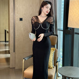 Woman wearing a long sleeve black midi dress with a sheer pearl-trimmed neckline.